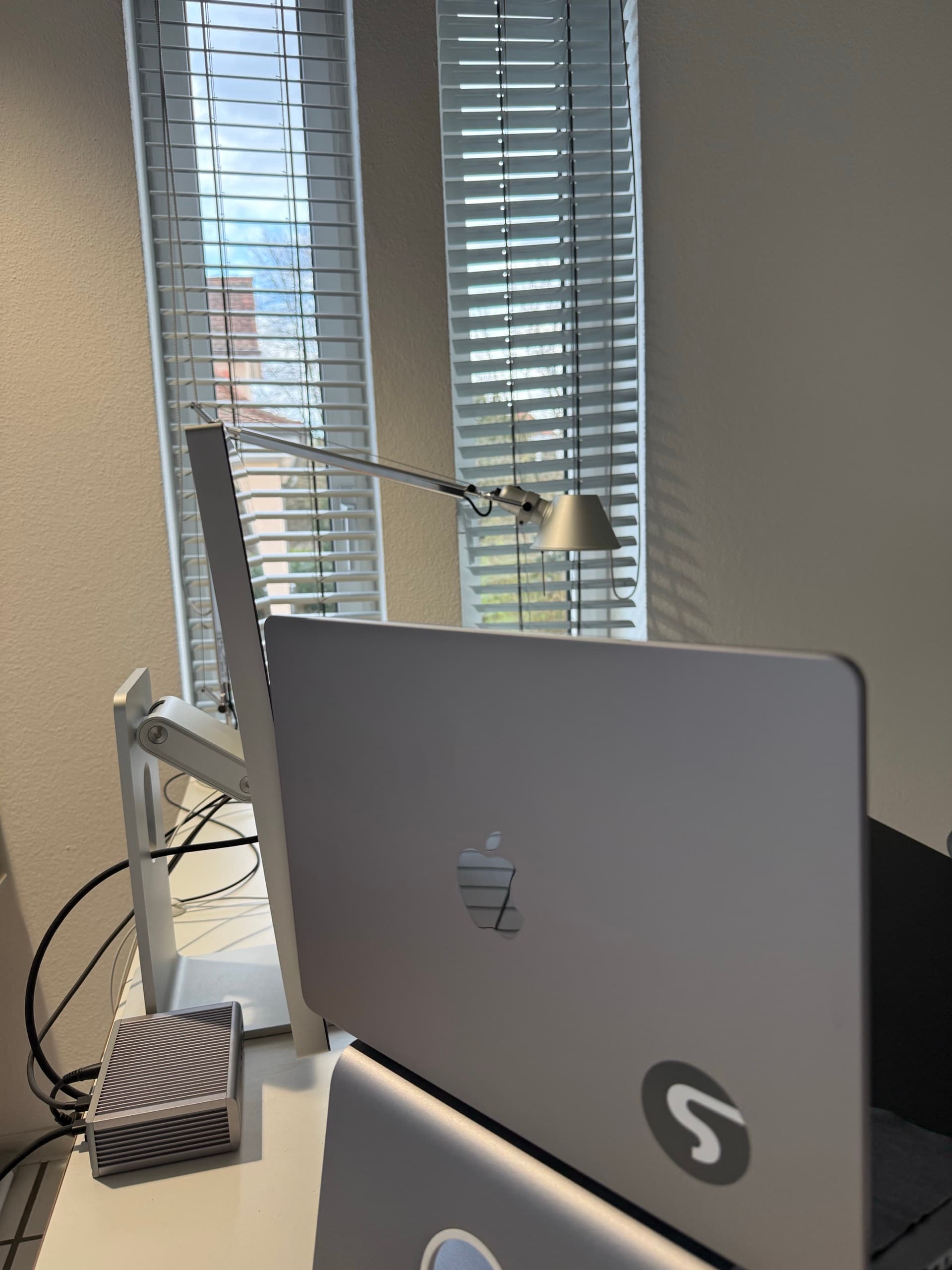 Arbeitsplatz im Studio: MacBook und Schreibtischleuchte vor einem Fenster mit Jalousien